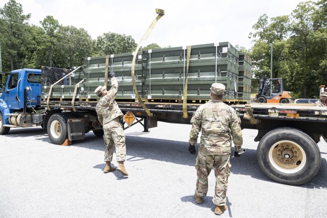Spc. Ederick Felicianomaldonado (left) and Spc. Baldy Fonrodonaaubert (right) use trailer winch straps to secure munitions to the flatbed trailer prior to transport.