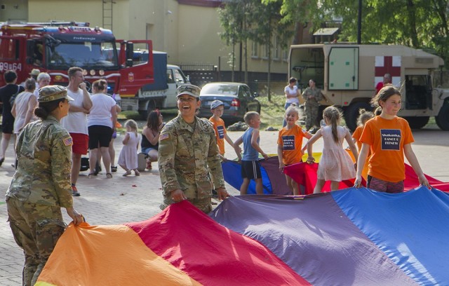 U.S. Army Pfc. Rebekah Rodriguez (foreground, left) and U.S. Army Staff Sgt. Ashley Peralta, both medics deployed with the 108th Medical Company Area Support, enjoy playing with local kids during a static display at a “Kupala Night” community...