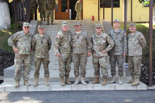 Col. Bigenho, Col. Calin, Maj. Gen. Baker, Col. Cristurean, Command Sgt. Maj. Boyd, Lt. Col. Brok, and Col. Blaga (pictured left to right) pose in front of the Joint National Training Center in Cincu, Romania.