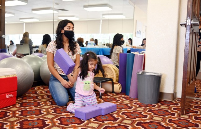 Marlen Lucero, a military spouse, listens during the Presidio of Monterey Military Spouse Orientation at the General Stilwell Community Center, Ord Military Community, Calif., Aug. 23, as her daughter, Scarlet, 2, plays.