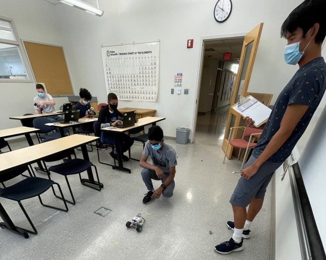 Students attending the “Robotics” GEMS program class at Hood College participate in an engineering exercise while a near-peer mentor (right) takes notes.
