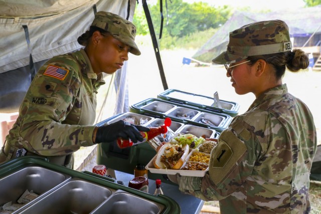 U.S. Army Spc. Ashely Ward (left), a culinary specialist to 511th Quartermaster Company, Special Troops Battalion, 1st Sustainment Brigade, 1st Infantry Division, serves a meal to U.S. Army 2nd Lt. Abigail del Rosario (right), 2nd platoon leader...