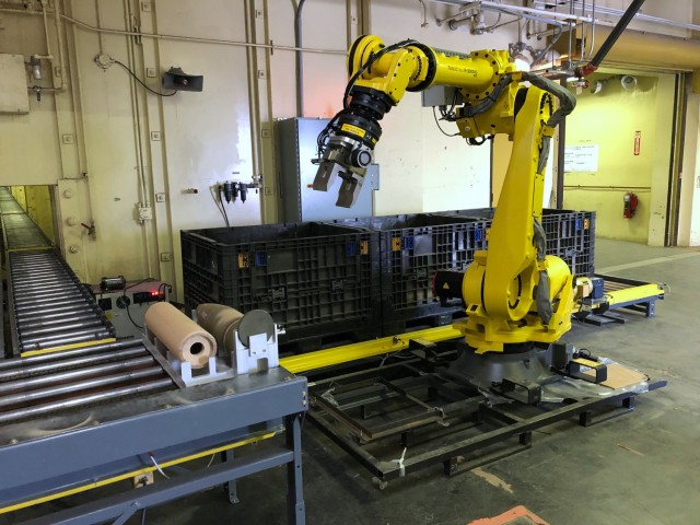 Automated packaging robot putting empty artillery shells in packages for shipment to recycling centers.