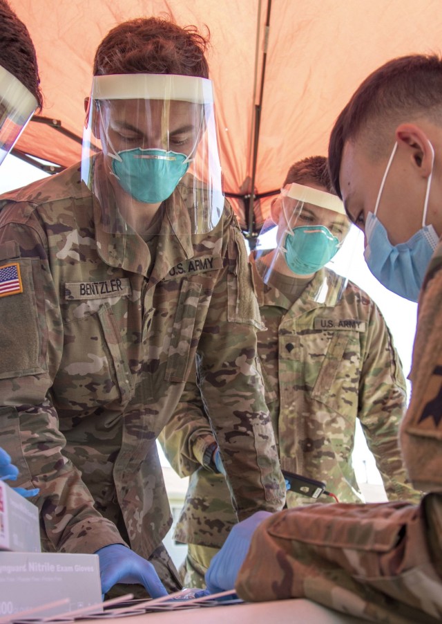 Spc. Kenneth Bentzler, left, a motor transport operator for 1157th Transportation Company, and Spc. Nash Brickl, right, an ammunition specialist for 641st Troop Command Battalion assigned to Task Force McCoy, prepare to conduct COVID-19 testing...
