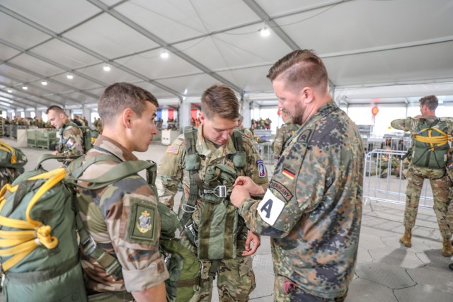 A German and a French soldier assist Sgt. John Brewer, Delta Company, 1st Battalion (Airborne), 143rd Infantry Regiment, in dawning a German parachute during Falcon Leap, Sept.15, 2021, at Eindhoven Air Base in the Netherlands.  The exercise...