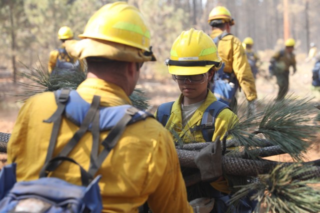 U.S. Army Pfc. Alexandria Reid, from 23rd Brigade Engineer Battalion, 1-2 Stryker Brigade Combat Team, assigned to Joint Base Lewis-McChord, Washington, hands off a pile of recently cut down tree branches to her teammate to avoid the potential spread of fire while deployed in support of the Department of Defense wildland firefighting response on the Dixie Fire in Lassen National Forest, California, Sept. 17, 2021. U.S. Army North, U.S. Northern Command’s Joint Force Land Component Command remains committed to providing flexible DoD support to the National Interagency Fire Center to respond quickly and effectively to assist our local, state, and federal partners in protecting people, property, and public lands.