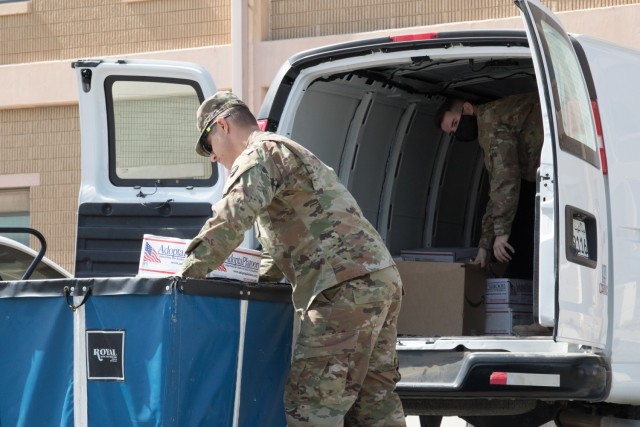 Spc. Joby L. Forney, a chemical, biological, radiological and nuclear specialist, lifts a parcel to hand to Cpl. Brett D. Ellis, a human resources specialist, outside of the post office at Camp Arifjan, Kuwait, on Oct. 2, 2021. The Soldiers, assigned to the Fort Bragg, North Carolina, based Headquarters and Headquarters Company, 3rd Expeditionary Sustainment Command, are two of several Soldiers who deployed to Kuwait in August to staff the 1st Theater Sustainment Command Operational Command Post.