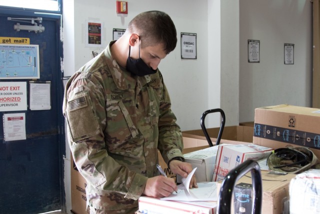 Spc. Joby L. Forney, a chemical, biological, radiological and nuclear specialist assigned to the Fort Bragg, North Carolina, based Headquarters and Headquarters Company, 3rd Expeditionary Sustainment Command, signs documents at the post office on Camp Arifjan, Kuwait, on Oct. 2, 2021. Forney, a native of Bend, Ore., is one of many Soldiers who deployed to Kuwait in August to staff the 1st Theater Sustainment Command Operational Command Post.