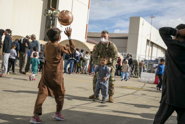 Sgt. First Class Robinson, a platoon sergeant assigned to 1st Battalion, 77th Field Artillery Regiment, plays a game with 2 Afghani children in the courtyard on Sept. 30, 2021 at Ramstein Air Base, Germany. Approximately 175 Soldiers from 1-77 FAR, 41st Field Artillery Brigade have been assigned to support Operation Allies Welcome and augment the security force at the holding facilities at Ramstein providing life support for Afghan travelers awaiting follow on flights. (Official U.S. Army photo by Spc. Ryan Barnes)