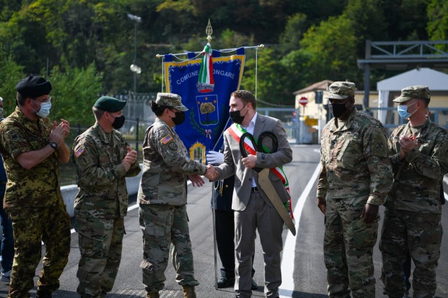Holding ceremonial scissors, Longare Mayor Matteo Zennaro shakes hands with Brig. Gen. Aida T. Borras, Deputy Commander of U.S. Army Southern European Task Force-Africa, as U.S. and Italian military look on, during an Oct. 4 opening of Via dei Martinelli, a local road outside the Longare post that was rebuilt with safety in mind.