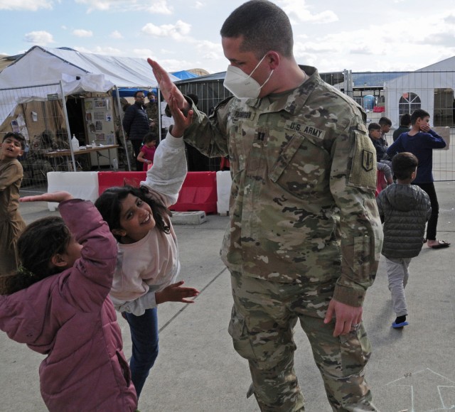 Cpt. Micah Thompson, the commander for Alpha Battery, 1st Battalion, 77th Field Artillery Regiment, get a high five young afghan girl as she waits to enter the enter the temporary school house at Ramstein Air Base, Germany on Sept. 30, 2021. Approximately 175 Soldiers from 1-77 FAR, 41st Field Artillery Brigade have been assigned to support Operation Allies Welcome and augment the security force at the holding facilities at Ramstein providing life support for Afghan travelers awaiting follow on flights. (Official U.S. Army photo by Maj. Joe Bush)