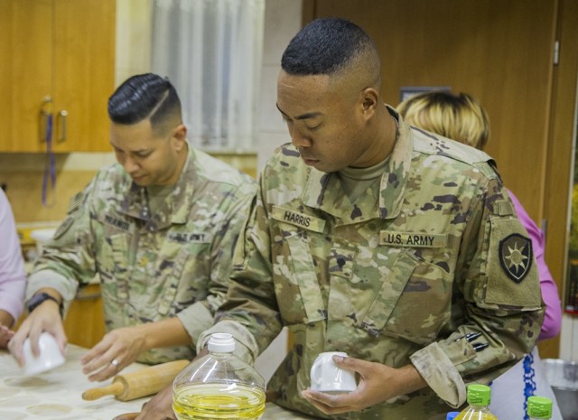 U.S. Army Maj. Joshua Franqui (left), director of intelligence, and Spc. Lamar Harris , intelligence analyst, use cups to cut dough that will be used for making pierogies under the supervision of members of a local women’s organization at the...