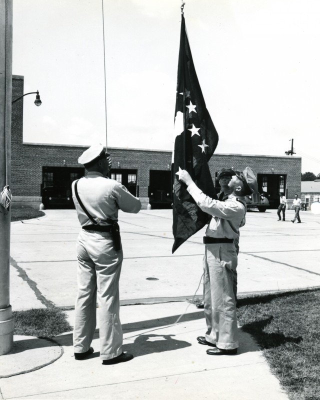 Security guards perform retreat of the colors at the Headquarters building, which was located across from the Fire Station.  The current Headquarters building  at Anniston Army Depot was constructed in 1975 and completed in 1977. 