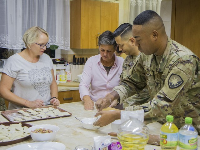 U.S. Army Spc. Lamar Harris (right), an intelligence analyst, and Army Maj. Joshua Franqui, director of intelligence, prepare dough for pierogies under the supervision of Mariola Waszak (left) and Miroslawa Kaluzinska at the Powidz Community...