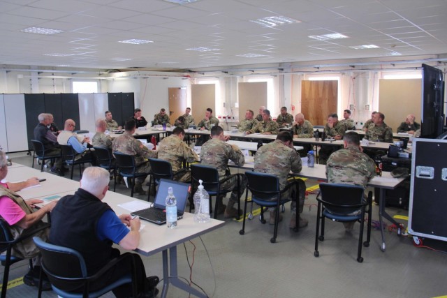 Leaders, senior mentors, and observer-coach trainers from Operations Group A, Mission Command Training Program, conduct an “azimuth check” meeting, October 4, 2021, at Grafenwoehr Training Area in Germany during warfighter exercise 22-1. The meeting was a daily briefing on the progress of the training audience’s battle against the World-Class OPFOR. The exercise involved V Corps commanding the Army's 3rd Infantry Division and 34th Infantry Division in a large-scale combat operations scenario against a peer threat, notionally based in Europe. (The personnel depicted were all vaccinated and had negative COVID testing results before the exercise.)