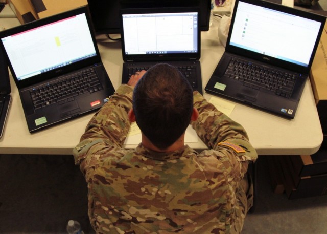 Sgt. Kyle Plumley, an intelligence analyst for Joint Force Headquarters, works three laptop computers at Camp Atterbury, Ind. 