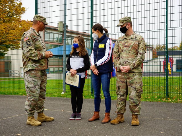 Col. Mario Washington, U.S. Army Garrison Wiesbaden garrison commander,  speaks to 5th grader Olivia Briggs and her parents as part of a recognition at Aukamm Elementary Oct. 18, 2021. Olivia was recognized for her efforts and her quick call to emergency services, preventing further fire danger at a nearby residence.
