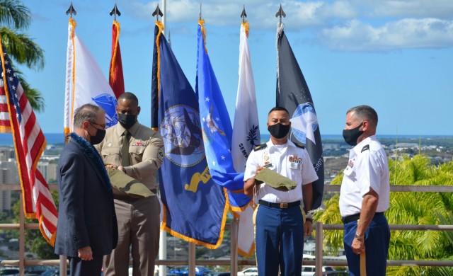 DHA Assistant Director Dr. Brian Lein (left), and Hawaii Market Director Col. Martin Doperak (right) prepare to unfurl the flags during the formal Hawai'i Market Establishment Ceremony.