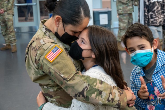 Sergeant 1st Class Jasmin Kissane hugs her daughter while her son photobombs at the Army Aviation Support Facility in Windsor Locks, Conn. on Oct. 24, 2021. Kissane's unit, the 142nd Medical Company, was mobilizing in support of Operation Atlantic Resolve and heading to Texas before deploying to Poland.