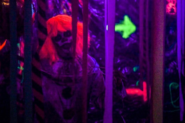 A volunteer clown lurks behind the streamers at the House of Fears haunted house during the Camp Humphreys Halloween Spooktacular, hosted by the Family and Morale, Welfare, and Recreation office and Better Opportunities for Single Soldiers program, at Sitman Gym parking garage Oct. 30, 2021. (U.S. Army photo by Spc. Brooke Davis)