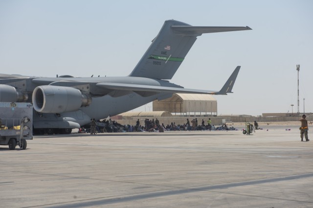 Qualified evacuees wait under the wing of C-17 Globemaster lll before they are able to process onto the aircraft, Aug. 20, 2021. As part of Operation Allies Refuge, Afghan citizens evacuated Hamid Karzai International Airport, Kabul, onboard...