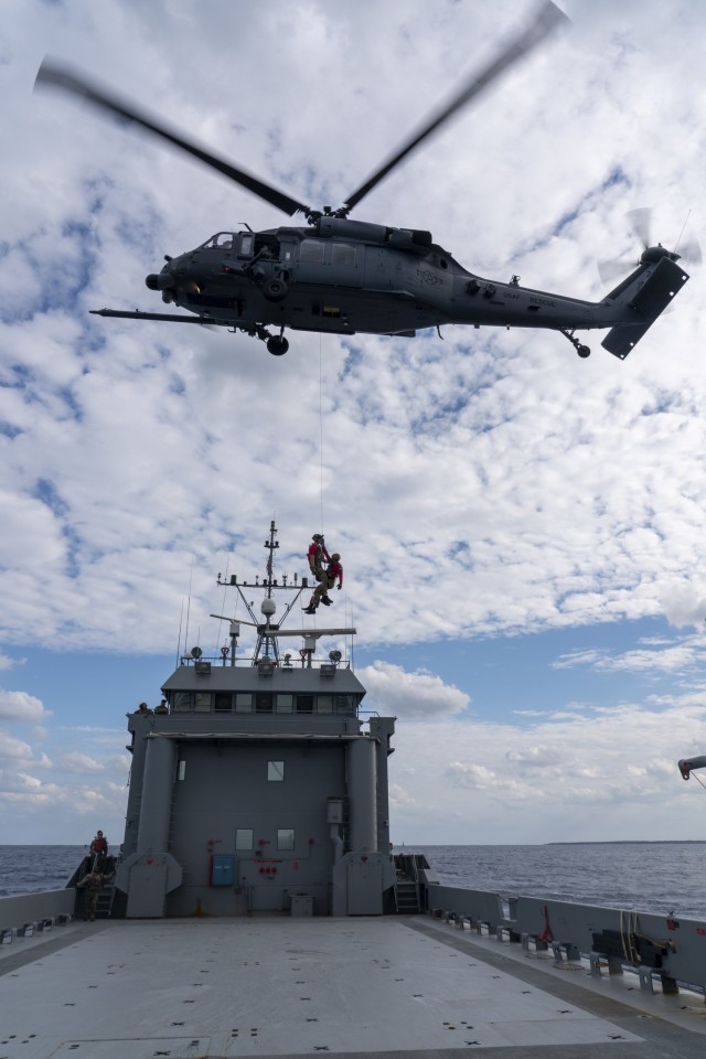A HH-60G Pave Hawk helicopter, assigned to the 33rd Rescue Squadron, hoists two pararescuemen from the 31st Rescue Squadron onto United States Army Vessel Landing Craft Utility 2020 (Fort McHenry), 10th Support Group, during joint training off the coast of Okinawa, Japan, Nov. 10. The exercise allowed both Army and Air Force units to gain the capability of medically evacuating patients off of the LCUs from sea.
