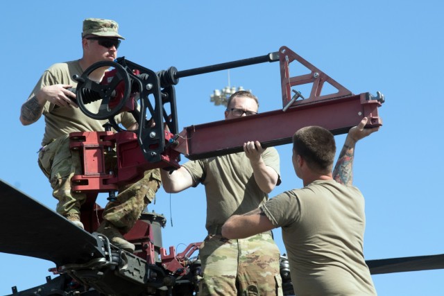 (Left to Right) Spc. Joseph R. Senn, Spc. Perry L. Harney, and 1st Sgt. Adam S. Castrogiovanni, assigned to the Fort Bragg, North Carolina, based 82nd Combat Aviation Brigade, 82nd Airborne Division, assemble equipment to fold the rotor blades of an AH-64E Apache helicopter at the Port of Shuaiba, Kuwait, Nov. 10, 2021. The Aberdeen Proving Ground, Maryland, based 1100th Theater Aviation Sustainment Maintenance Group oversaw the preparations for the retrograde of more than 30 aircraft assigned to the 82nd CAB from Nov. 7-12. The Soldiers and aircraft were deployed to Afghanistan to support base closures and the U.S. military’s exit from the Hamid Karzai International Airport in Kabul.