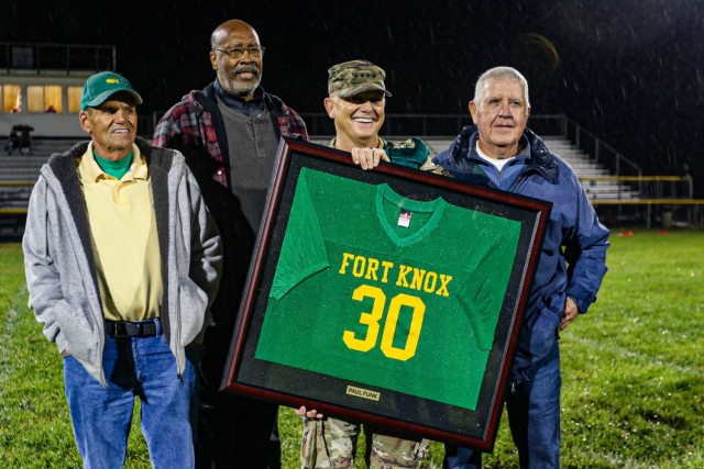 General Paul Funk II holds his retired football jersey with his former coaches at Fort Knox Middle/High School October 29. The Fort Knox Eagles honored Funk, commanding general, U.S. Army Training and Doctrine Command, and former Eagle football star, with a jersey retirement ceremony during halftime of the final game of the 2021 season. Funk's former coaches surprised him by attending the leader's homecoming ceremony and he attributed his initial leadership training to his mentors. Funk's wife, youngest son, and other family members and friends were in attendance for the momentous occasion. (U.S. Army photo by Staff Sgt. Nicholas Brown-Bell)