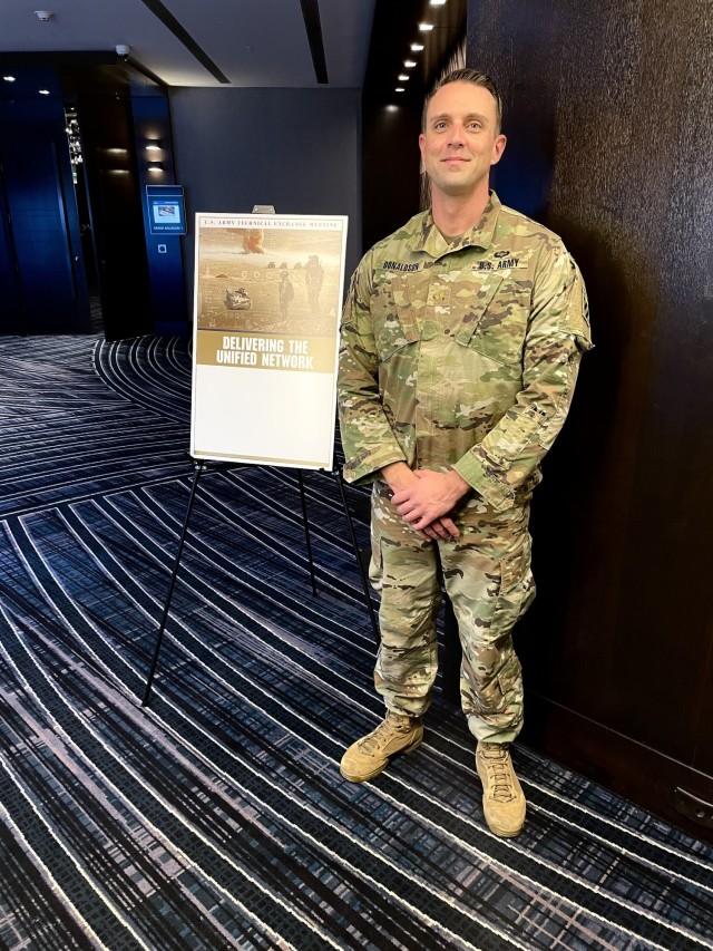 Maj. Todd Klinzing-Donaldson, the top network and communications officer for the "Spartan Brigade," 2nd Armored Brigade Combat Team, 3rd Infantry Division, poses in front of the "U.S. Army Technical Exchange Meeting 7: Delivering the Unified Network,” billboard after speaking on the “Warfighter Perspective: Networking to Support the MDO Concept” panel in Nashville, Tennessee, Dec. 2, 2021. The Spartan Brigade is the supporting unit for the Army’s upcoming ABCT On-The-Move network communications pilot and together with the 3rd ID leadership provided feedback and insight to industry on pilot requirements and desired outcomes. (U.S. Army photo by Capt. Sean Minton)
