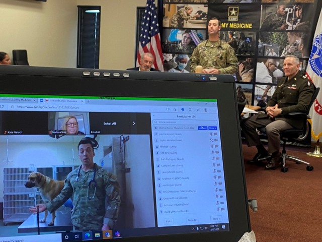Sgt. 1st Class Dylan Browning (foreground), 68T Animal Care Specialist, alongside Laager, a canine patient, describes his reasons for serving and the benefits of his career choice via zoom to an audience of high school students from over 40 schools across Texas during the U.S. Army Medical Center of Excellence, or MEDCoE, Virtual Career Showcase, December 6, 2021. In the background, Sgt. 1st Class Sean Skaggs, 68C Nursing Specialist (center) waits to brief the group alongside hosts Maj. Gen. Dennis LeMaster (far right), MEDCoE Commanding General; Joseph Bray, Civilian Aide to the Secretary of the Army-Texas, South (far left).