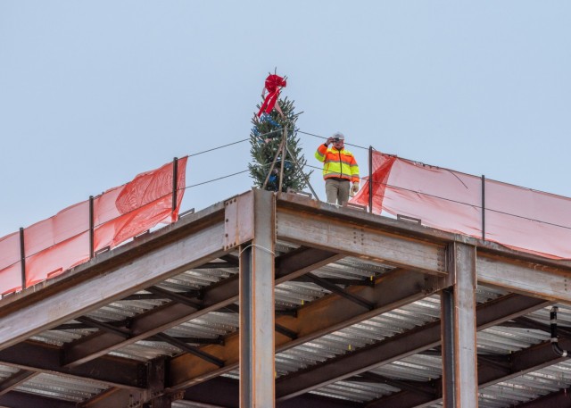 A construction worker takes a photo of the illuminated tree at the highest point of the new General Leonard Wood Army Community Hospital construction site. The tradition of placing a tree at the highest point of a new structure dates back to Scandinavian lore. The goal being to bring good luck to the remainder of the project and good fortune to the future inhabitants of the completed structure.