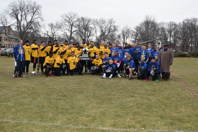 The Army flag football team proudly displays the trophy they had just earned by defeating the Navy flag football team, all those involved standing united after playing as adversaries the afternoon of Dec. 3 on Memorial Field at Rock Island...