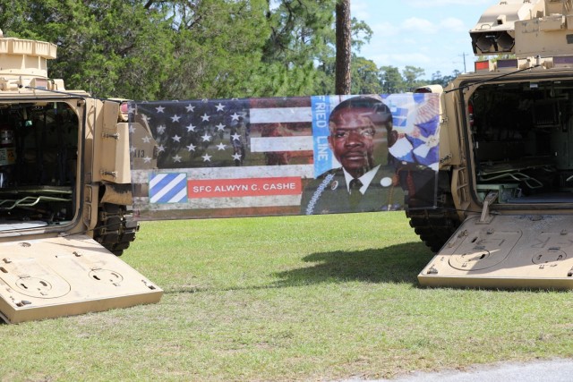 A banner with a photograph of Sgt. 1st Class Alwyn Cashe hangs between two Bradley Fighting Vehicles as part of a static display during the dedication ceremony for Sgt. 1st Class Alwyn C. Cashe Garden on Fort Stewart, Georgia, May 20, 2021. 3rd Infantry Division dedicated the ceremonial garden to honor the Dogface Soldier, leader and Silver Star Medal recipient, and to inspire others to emulate his example. Cashe will be posthumously awarded the Medal of Honor and it will be presented to his family during a ceremony scheduled for Dec 16, 2021. (U.S. Army Photo by 3rd Infantry Division Public Affairs)