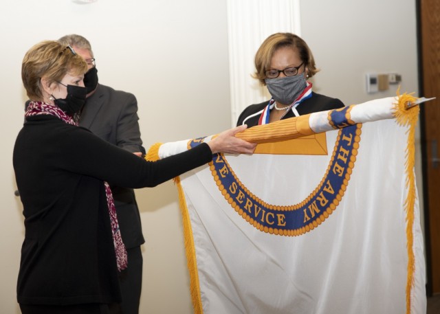 Carol Burton (left), director of the Civilian Human Resources Agency, unfolds the Senior Executive Service flag presented to Hong Miller, CHRA deputy director, during her SES promotion ceremony held at Rock Island Arsenal, Illinois, Dec. 8. (Photo by Linda Lambiotte, ASC Public Affairs)