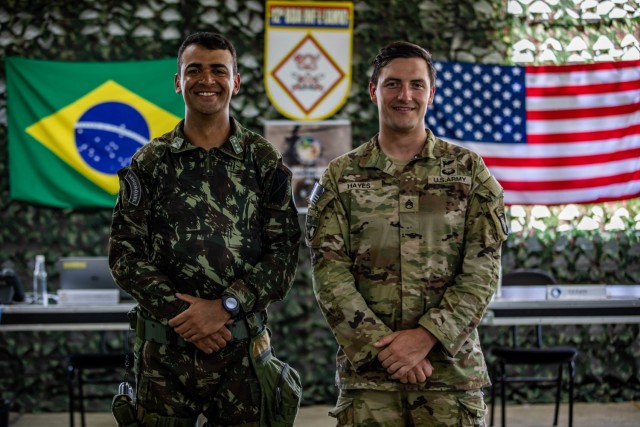 U.S. Army Soldier Staff Sgt. Shane Hayes, weapons squad leader with Bulldog Company, 1st Battalion, 187th Infantry Regiment, 3rd Brigade Combat Team, 101st Airborne Division (Air Assault) and Brazilian Army Soldier Maj. Rafael Marcos da Costa Ribeiro, assistant G3 operations officer assigned to 12th Light Infantry Brigade (Air Assault), 2nd Division, stand in front of their respective flags during Exercise Southern Vanguard 22 in Resende, Brazil, Dec. 14, 2021. U.S. and Brazilian Army soldiers took part in the air assault exercise, which was the largest deployment of a U.S Army unit to train with the Brazilian Army forces in Brazil. (U.S Army photo by Pfc. Joshua Taeckens)