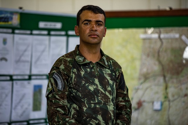 Brazilian Army Soldier Maj. Rafael Marcos da Costa Ribeiro, assistant G3 operations officer assigned to 12th Light Infantry Brigade (Air Assault), 2nd Division, stand in front of their respective flags during Exercise Southern Vanguard 22 in Resende, Brazil, Dec. 14, 2021. U.S. and Brazilian Army soldiers took part in the air assault exercise, which was the largest deployment of a U.S Army unit to train with the Brazilian Army forces in Brazil. (U.S Army photo by Pfc. Joshua Taeckens)