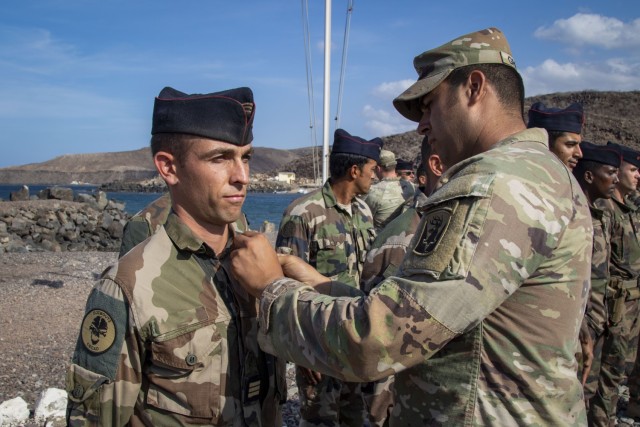 U.S. Army Staff Sgt. Alexander Griffith, 1-102nd Infantry Regiment, Task Force Iron Gray, Combined Joint Task Force - Horn of Africa (CJTF-HOA), pins a Ram's Head device on a French service member during a graduation ceremony at the French Combat...