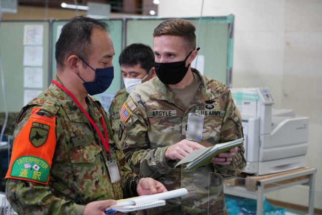 Capt. Jonathan Argyle, an observer-coach-trainer (OC/T) with the Mission Command Training Program (MCTP), speaks with a Japanese service member and interpreter to coordinate training between the forces during Yama Sakura, a joint bilateral military exercise with the Japan Ground Self-Defense Force, 1-12 December 2021, conducted across multiple camps in Japan. MCTP delivered a contingent of observer-coach-trainers (OC/T) to support the training alongside Australian and Japanese OC/T teams.