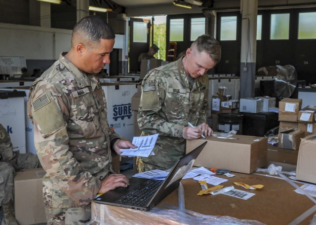 Staff Sgt. Alexis Alvelo with SSA Platoon, Atlas Distribution Company, 101st Brigade Support Battalion, 1st Armored Brigade Combat Team, 1st Infantry Division, and Staff Sgt. Kelly, an augmentee, process items by shipping labels. Receiving is one...