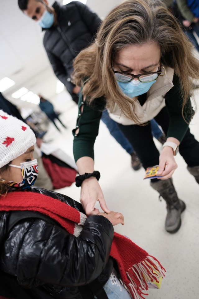 Rosana Resende, Deputy Lead for U.S. State Department at Task Force McCoy, gives an Afghan child of the last family to depart Fort McCoy, Wisconsin, a sticker as they prepare to board to the bus, Feb. 15, 2022. The Department of Defense, through U.S. Northern Command, and in support of the Department of Homeland Security, is providing transportation, temporary housing, medical screening, and general support for at least 50,000 Afghan guests at suitable facilities, in permanent or temporary structures, as quickly as possible. This initiative provides Afghan guests essential support at secure locations outside Afghanistan. (U.S. Army photo by Sgt. Robert P Wormley III, 50th Public Affairs Detachment)