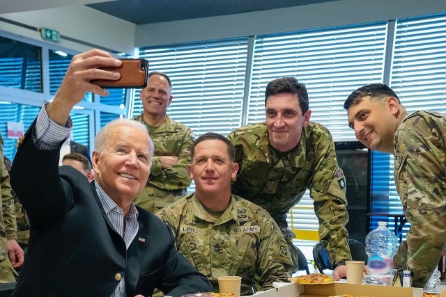 President Joe Biden holds up a phone to snap a selfie with smiling soldiers