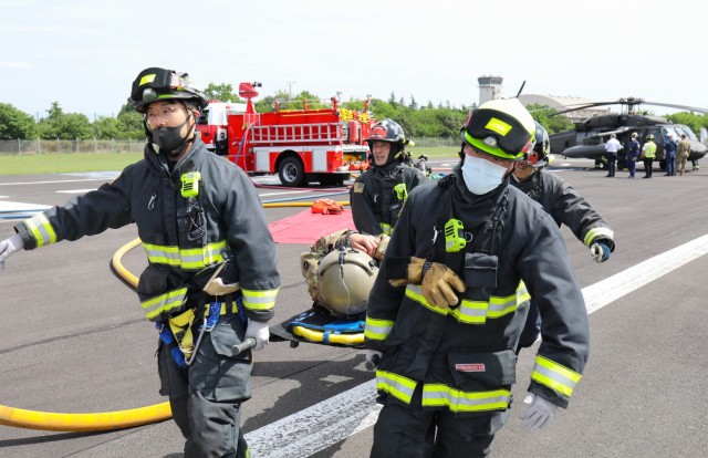 Firefighters from the U.S. Army Garrison Japan Fire Department use a litter to carry Chief Warrant Officer 4 Joseph Mattos to safety during a mock aircraft crash at Kastner Airfield, Camp Zama, Japan, April 28, 2022. Mattos, the aviation maintenance officer for U.S. Army Aviation Battalion Japan, was one of the pilots of a UH-60 Black Hawk helicopter that simulated a crash landing.
