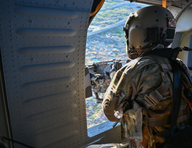 Army Specialist Arthur Allen, assigned to the 3rd Battalion, 142nd Aviation Regiment of the New York National Guard, fires an M240B machine gun from a hovering UH-60L Black Hawk helicopter at Fort Drum, New York, April 28, 2022, during annual training. The battalion is preparing to mobilize in June and deploy to Kuwait. (New York Army National Guard photo by Staff Sgt.Matthew Gunther)