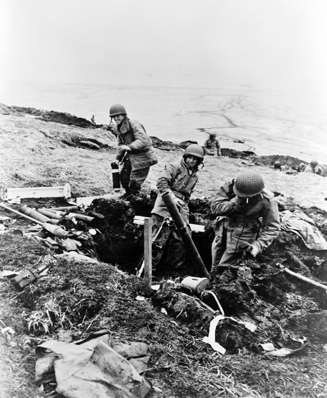 Soldiers hurling their trench mortar shells over a ridge into a Japanese position at Attu, Aleutian Islands.