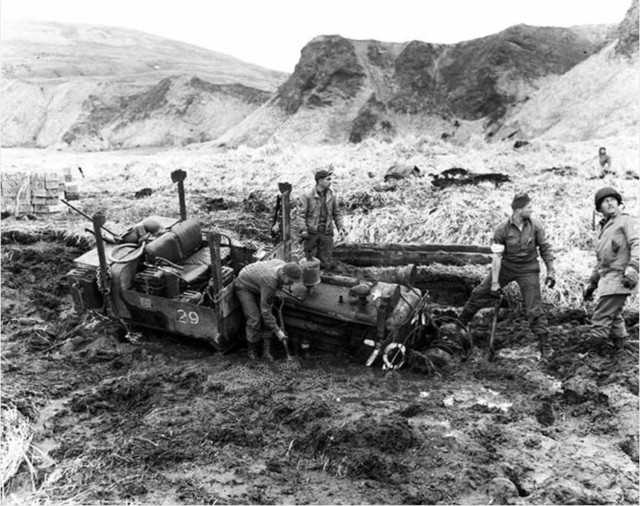 American soldiers dig a tractor from the mud.