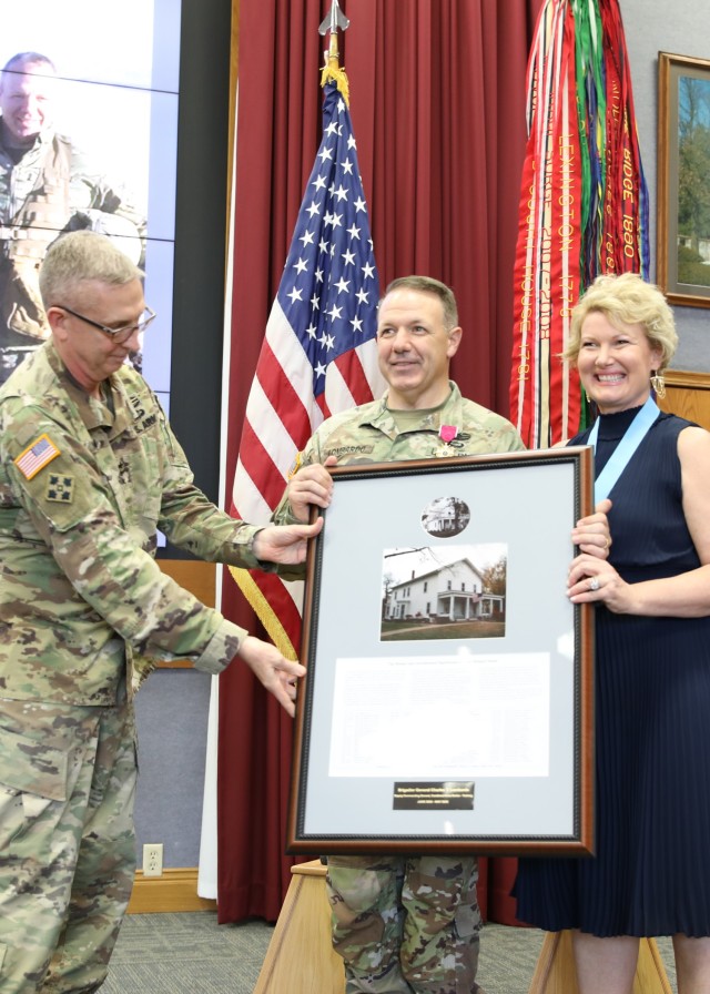 Combined Arms Center Commanding General Lt. Gen. Theodore Martin presents Combined Arms Center-Training Deputy Commanding General Brig. Gen. Charles Lombardo and his wife Kristy Lombardo with a framed photo and list of previous occupants of their historic Fort Leavenworth quarters during the Lombardo’s farewell and award ceremony May 11, 2022 in Grant Auditorium, Fort Leavenworth, Kan.  Photo by Tisha Swart-Entwistle, Combined Arms Center-Training Public Affairs.
