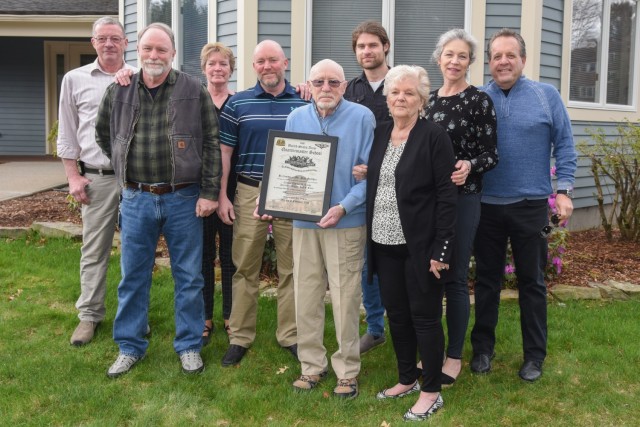 Retired DEVCOM Soldier Center civilian employee Peter Stalker holds his award while posing with his family at his home in Massachusetts after an April 27 presentation honoring his recent induction into the U.S. Army Quartermaster School Parachute Riggers Hall of Fame.