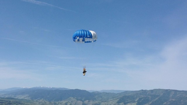 A smokejumper with a round parachute uses the steering toggles to hit their landing spot.