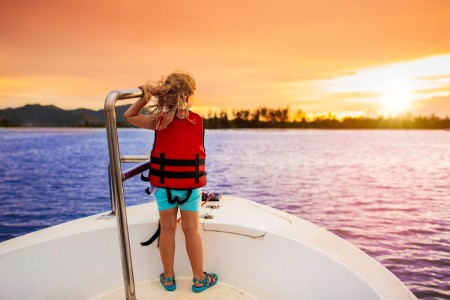 girl wearing a red life jacket and looking out at the sunset.