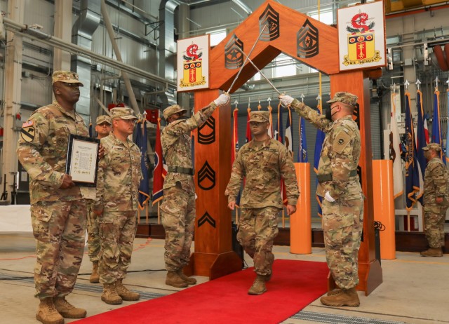 Sgt. Ulises Huang, center right, walks under a wooden arch adorned with all the enlisted ranks and a pair of raised sabers to be officially inducted into the NCO corps during a ceremony at Sagami General Depot, Japan, June 10, 2022.